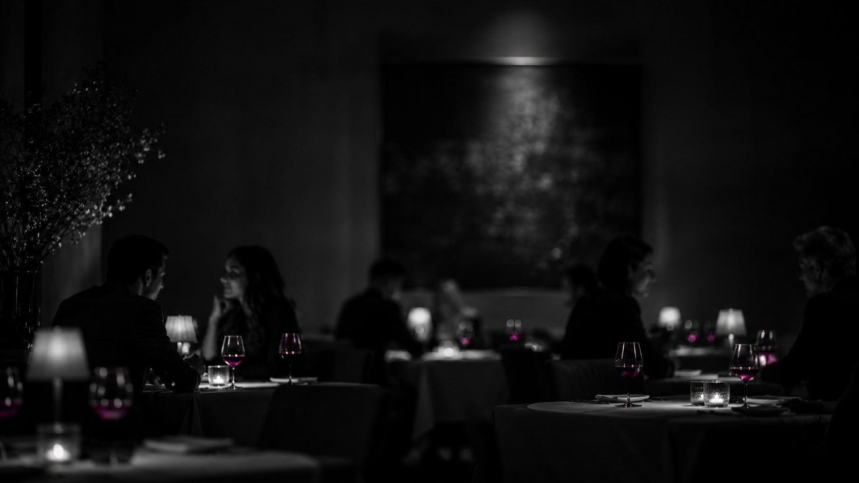 Dunkler Restaurantsaal bei Nacht, Schwarzweiß, die Weingläser leuchten magenta