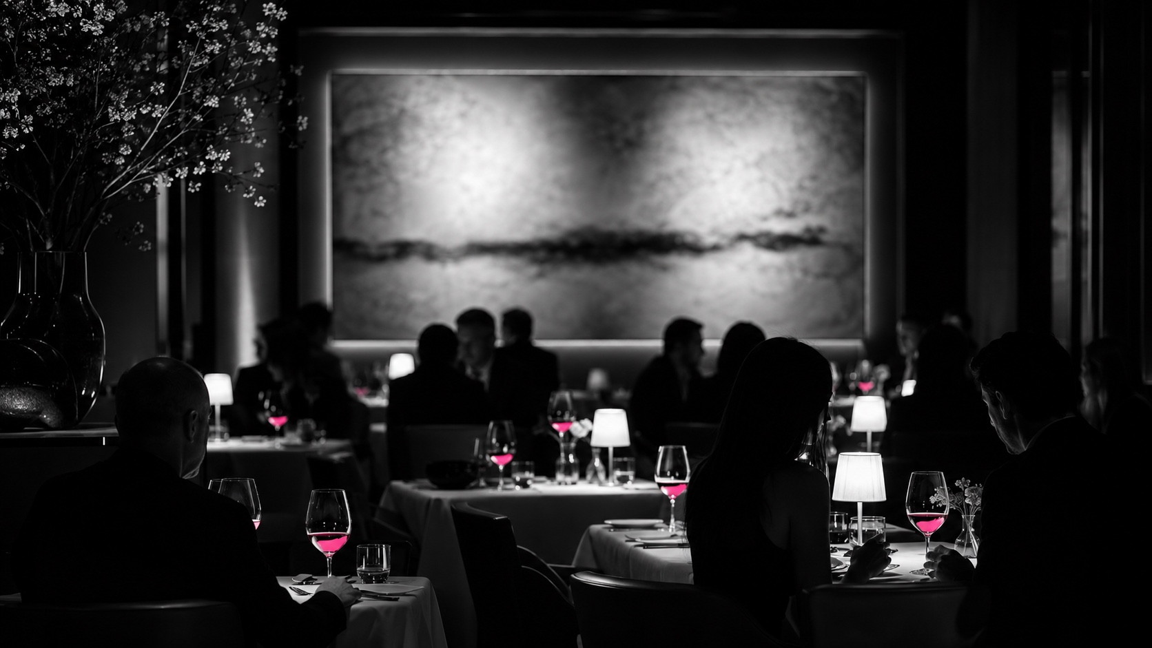 Sala de un restaurante en penumbra por la noche, en blanco y negro, las copas de vino brillan en magenta