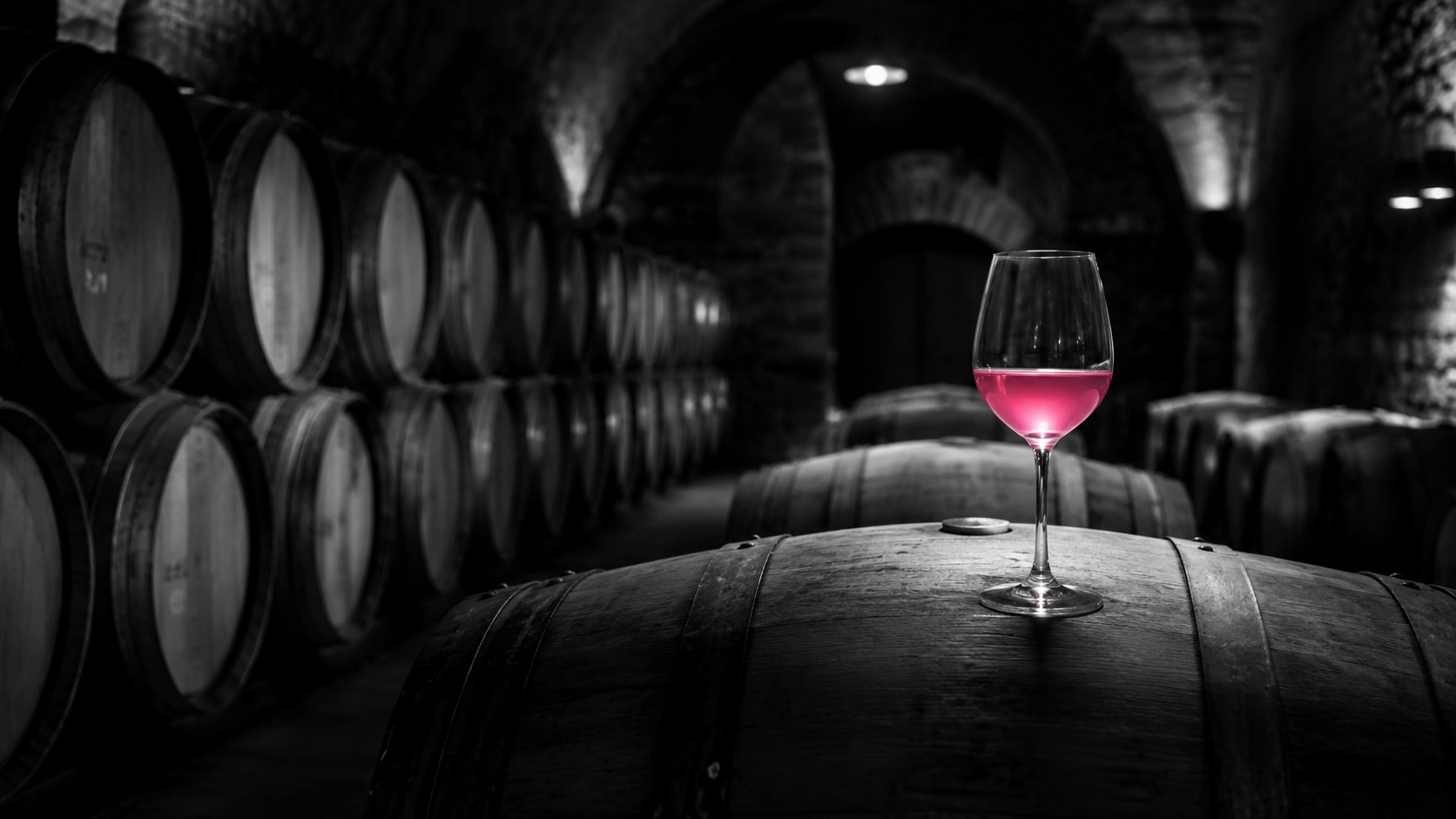Eichenfässer im dunklen Weinkeller, Schwarzweiß, ein Glas Chardonnay leuchtet magenta