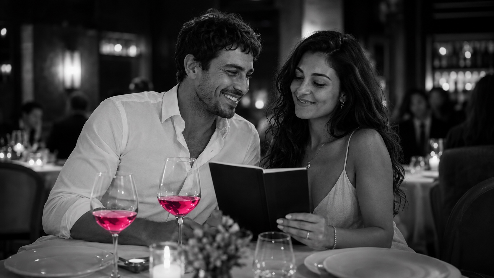 Giulia e il suo compagno chinati sulla carta dei vini al ristorante, in bianco e nero, il vino brilla di magenta