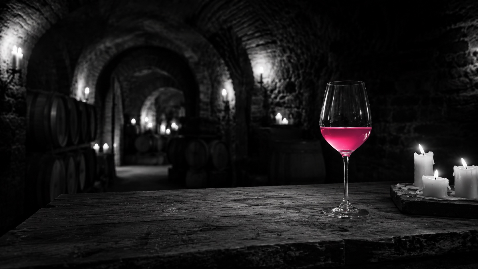 Rotweinglas im kerzenbeleuchteten Gewölbekeller, Schwarzweiß, der Wein leuchtet magenta